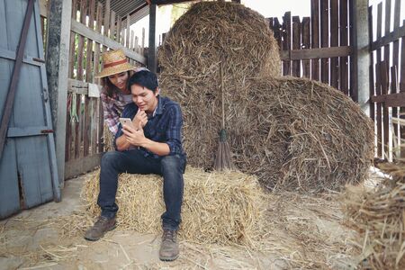 Farming couple with laptop,smartphone in hay shed.の写真素材