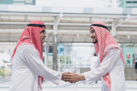Two Arabic men having warm meeting with a hug and handshakes, modern city background