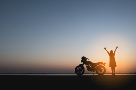 Silhouette of  woman and motorbike on the hill with sunset background, enjoying freedom and active lifestyle, having fun on a bikers tourの写真素材