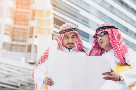 Arab businessman going over some blueprints with his engineer talking about job and verify the blueprint with commitment to success at construction site with building backgroundの写真素材