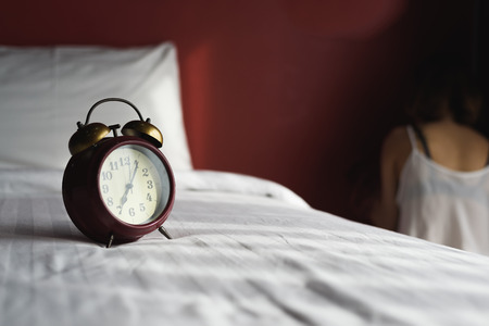 Retro alarm clock on the bed with woman sitting strain ,unhappy In the corner of the room, の写真素材