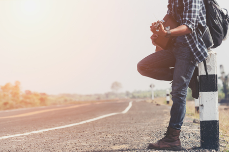 Man with Backpacks and Guitar in casual Travel Clothes walking along road ,Road hitch-hiking. Traveler standing at the highway hitchingの写真素材