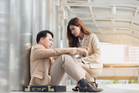 Feeling so hopeless. Young businesswoman comforting her boyfriend  while sitting together. Unhappy businessman being sad on the street in the cityの写真素材