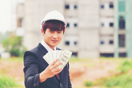 Engineer holding money on the building being under construction background, construction and architecture concept.の写真素材