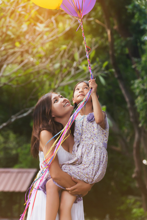 Happy mother and daughter with colorful helium balloons in parkの写真素材