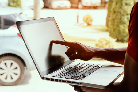 A man holding and pointing to a laptop screen with car park background.の写真素材