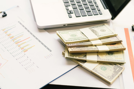 Stacks of money and laptop on the table And business documents.の写真素材