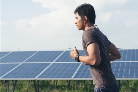 Cardio runner running listening smartphone music in a solar power plant. Sporty fit young man...
