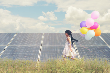 A funny girl carrying a colorful balloon running in a meadow with a Solar panel, photovoltaic. Concept of Eco-Friendly ,Clean Energy , Pure energy and Sustainable energyの写真素材