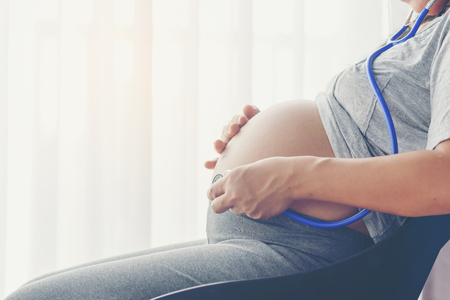 Pregnant woman with stethoscope listening belly to baby,Pregnancy and motherhood conceptの写真素材