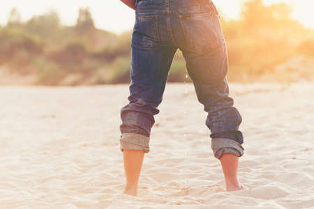 Standing man peeing on sand beach.