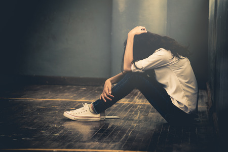 Lonely sad woman cry and hug her knees sitting in the dark corner ,Sad woman Unhappy and stressed student on the campus ,Family problems and education conceptの写真素材