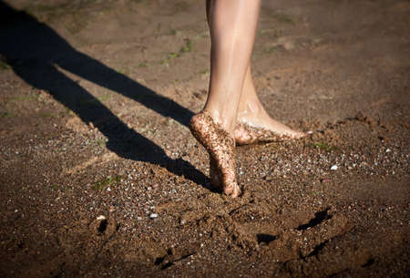 Girl's barefoot legs on the sand beach