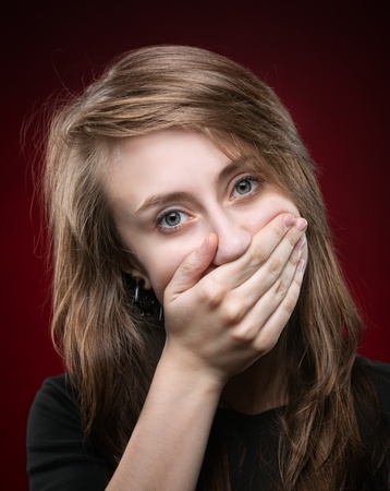 Beautiful young woman covering the face with her hand, on a dark red backgroundの写真素材