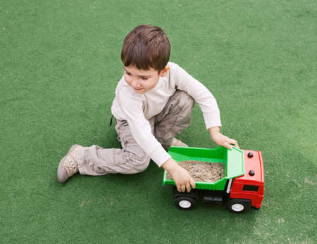 Smiling little boy plays on green grass with toy carの写真素材