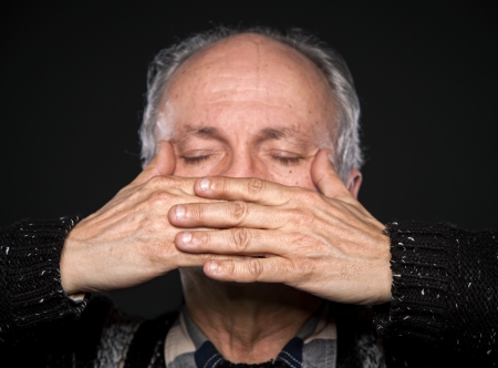 An elderly man with closed eyes closed mouth with hands. Focus on handsの写真素材