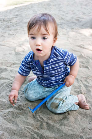 Cute emotive kid playing with toy and sand on playground