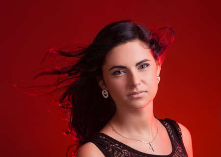 Beautiful young woman with hair blowing on wind on red backgroundの写真素材