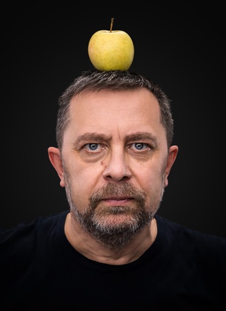 Portrait of a middle-aged man with a green apple on his headの写真素材
