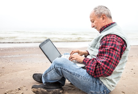 Old man sitting with notebook on sea beachの写真素材