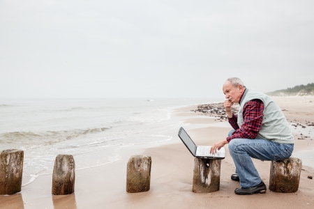 Senior businessman on beach working with notebook on a foggy dayの写真素材