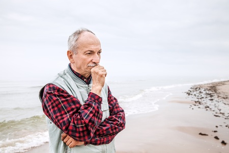 Thoughtful elderly man standing on the beach on a foggy dayの写真素材