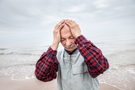 Elderly man suffering from a headache on sea background on foggy dayの写真素材