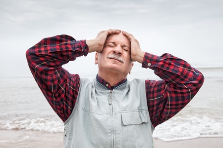 Elderly man suffering from a headache on sea background on foggy dayの写真素材