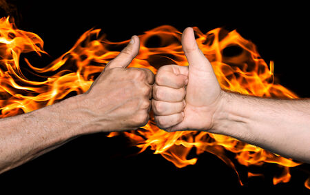 Friendship sealed with fire concept. Two men bumping fists with thumbs up against the fire flamesの写真素材