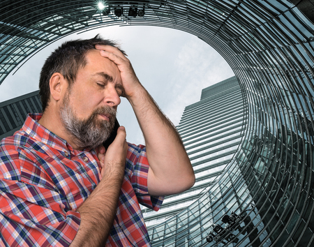 Hard talk. Middle-aged businessman talking on mobile phone in the megalopolisの写真素材
