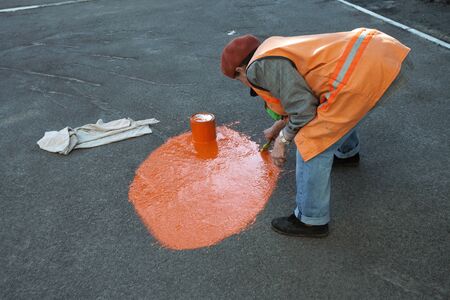 Street worker paints circle on asphalt by orange paint