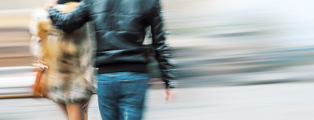 Man in jeans and a woman in a fur coat walking down the street hugging. Intentional motion blurの写真素材