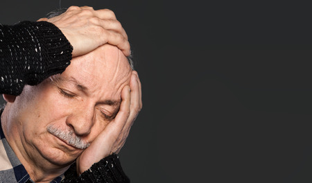 Elderly man suffering from a headache and toothache on gray background with copy-spaceの写真素材