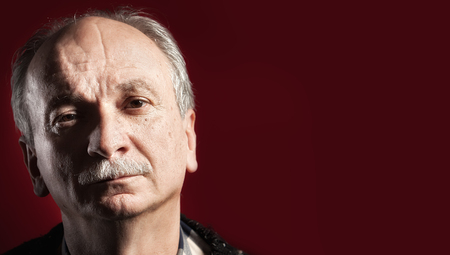 Portrait of handsome senior man with a tired expression on red background with copy-space