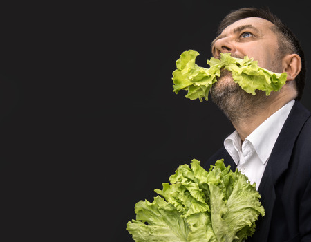 Healthy food. Man holding and eating lettuce on dark background with copy-spaceの写真素材