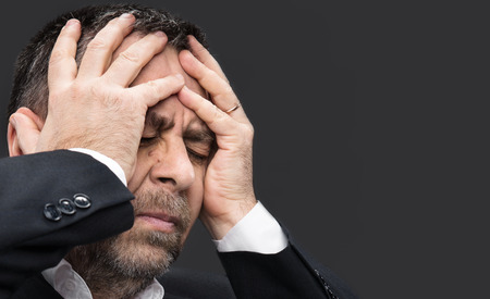Headache. Portrait of an elderly man with face closed by hands on dark background with copyspace