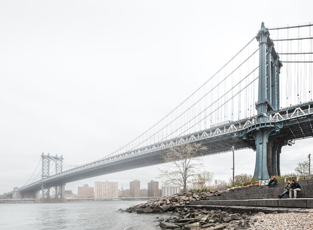 NEW YORK, USA - Apr 29, 2016: People relax on the shore of the East River against the Manhattan Bridge on a foggy dayのeditorial素材