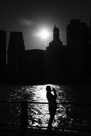 Silhouette of a young man the background of the East River and the setting sun with the skyscrapers of Manhattan in NYCの写真素材