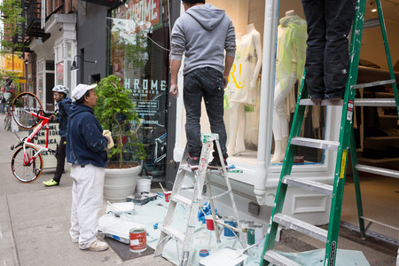 NEW YORK, USA - Apr 28, 2016: Manhattan street scene. Workers paint and repair the front of the ready-made clothing store. Cyclist in helmet in the backgroundのeditorial素材