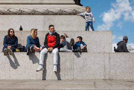 LONDON, UK - Apr 19, 2017: Adults and children rest at the base of the Nelson column. Nelson Column...