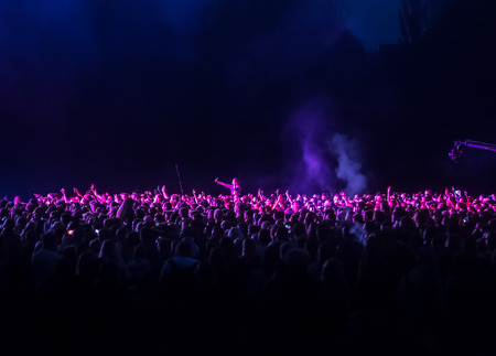 KIEV, UKRAINE - Jul 01, 2017: Crowd of spectators at a concert at night lit by a spotlight from the stage against a background of nature and dramatic storm cloudsのeditorial素材