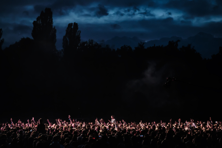 KIEV, UKRAINE - Jul 01, 2017: Crowd of spectators at a concert at night lit by a spotlight from the stage against a background of nature and dramatic storm cloudsのeditorial素材
