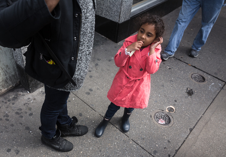 NEW YORK, USA - May 03, 2016: Manhattan street scene. A dark-skinned girl in a pink raincoat is standing on the sidewalk in the middle of Manhattanのeditorial素材
