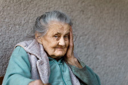 Portrait of a very old and tired of life wrinkled woman outdoors with a hand near her faceの写真素材