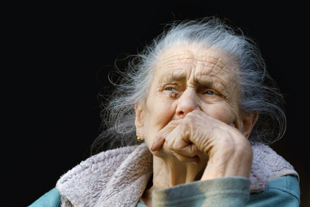 Portrait of a very old and tired of life wrinkled woman outdoors with a hand near her faceの写真素材