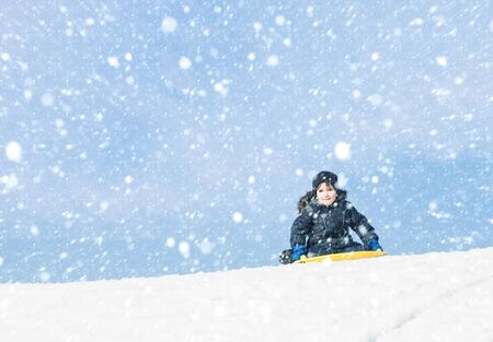 Lifestyle concept. Boy playing outdoors on a snowy winter day. Boy on sleigh. Sledding at winter...