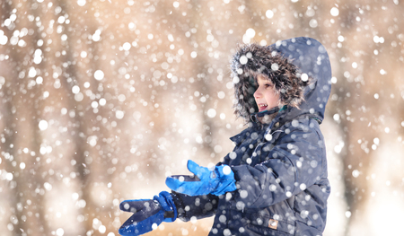 Cute boy playing with snow in the winter park  during a snowfall on a winter dayの写真素材