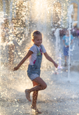 KIEV, UKRAINE - Jun 05, 2018: Cheerful and happy girl playing in a water fountain and enjoying the cool streams of water in a hot day. Hot summer.のeditorial素材