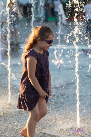 KIEV, UKRAINE - Jun 05, 2018: Cheerful and happy girl playing in a water fountain and enjoying the cool streams of water in a hot day. Hot summer.のeditorial素材