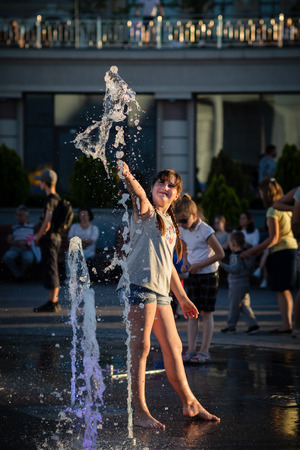 KIEV, UKRAINE - Jun 05, 2018: Cheerful and happy girl playing in a water fountain and enjoying the cool streams of water in a hot day. Hot summer.のeditorial素材